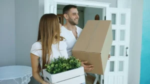 Pareja joven entrando con cajas en su primera vivienda comprada con el aval ICO 2026