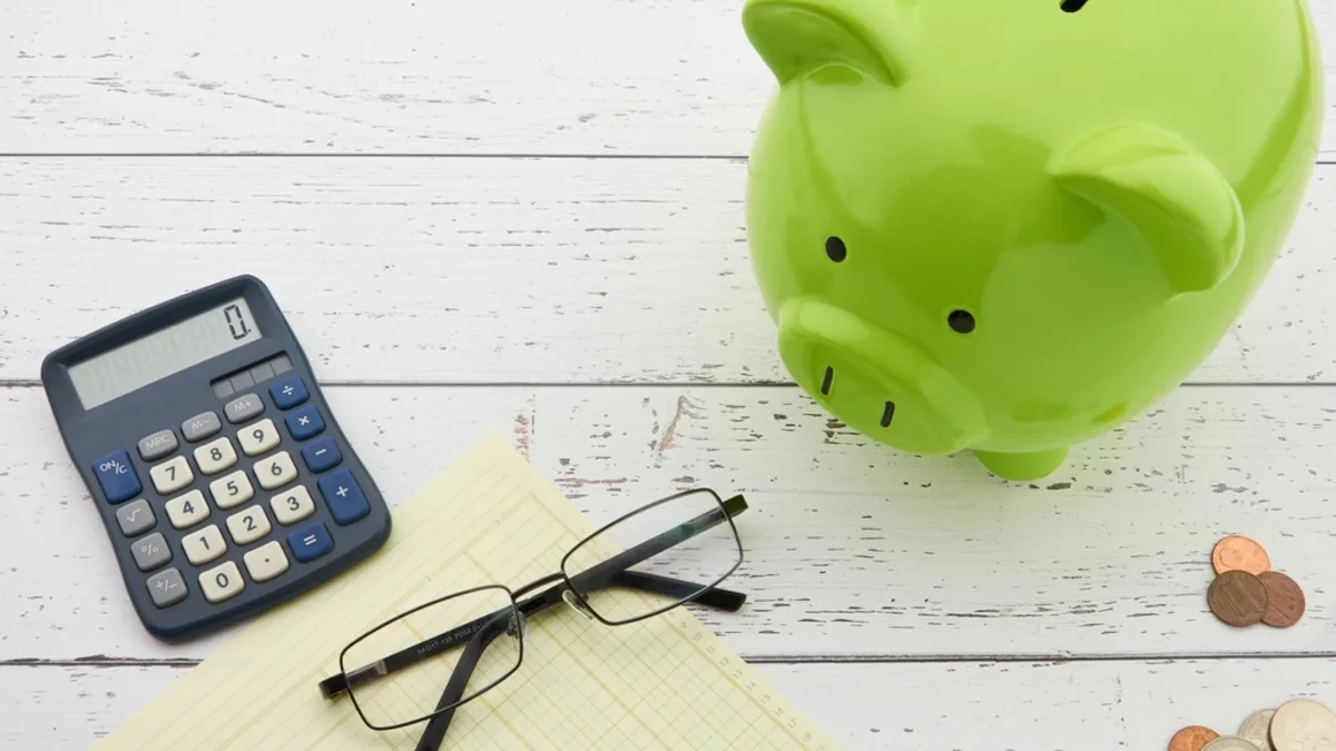 Hucha y calculadora sobre papeles: calcular si reducir cuota o plazo de la hipoteca